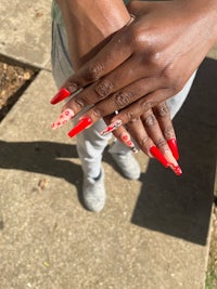 a woman holding a red nail with a flower design on it